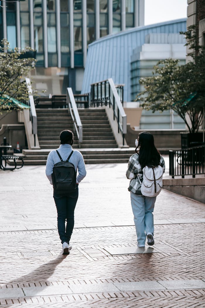 Back view of full length anonymous multiracial female students in masks with backpacks walking to stairs in campus